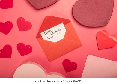 A flat lay Valentine’s Day composition on a pink background featuring red and pink heart-shaped gift boxes, envelopes, paper hearts, a ribbon bow, and a handwritten love note in an open envelope