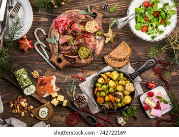 Flat Lay Of Delicious Christmas Themed Dinner Table With Roasted Meat Steak, Appetizers And Desserts. Top View. Holiday Concept.