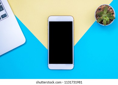 Flat lay design with blank on smart phone. Device laptop and plant on a yellow and blue background.  - Shutterstock ID 1131731981