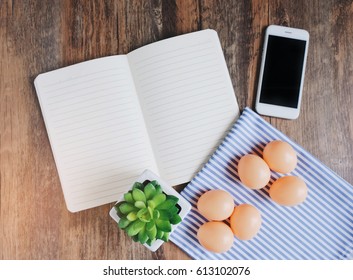 Flat lay design of notebook, smartphone, plant and eggs on wooden table background, spring concept