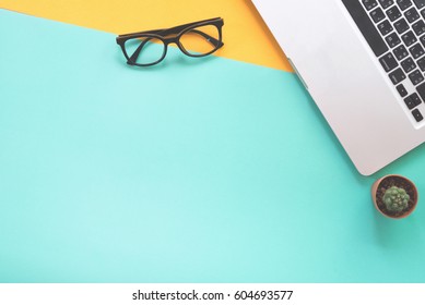 Flat Lay Design Of Work Desk With Notebook, Eye Glasses And Cactus On Green And Yellow Background. 