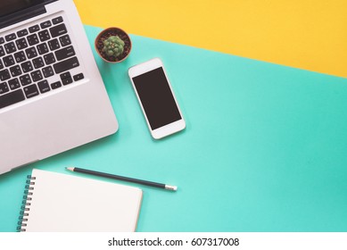 Flat Lay Design Of Work Desk With Labtop Notebook, Smartphone And Cactus On Green And Yellow Background. 