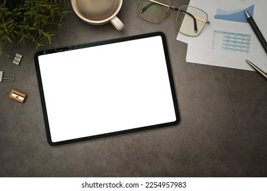 Flat lay digital tablet with blank screen, cup of coffee cup, glasses and notepad on black stone table - Shutterstock ID 2254957983