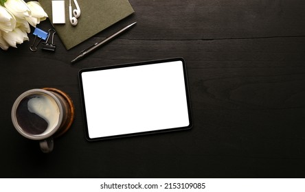 Flat lay digital tablet with empty screen, coffee cup and supplies on wood background.