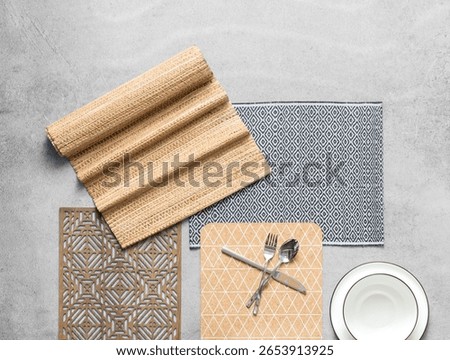 Flat Lay Dining Elegance: Burlap Textured Placemat, Intricate Wooden Trivet, Patterned Fabric Napkin, Crossed Silverware, and a Classic White Plate with Gold Trim on a Gray Polished Cement Background