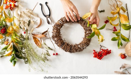 Flat lay with diy floral autumn wreath with dried grass, plant and berry with woman hands on white background, top view, copy space, banner