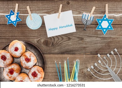 Flat Lay With Doughnuts, Candles, Menorah And Happy Hannukah Card On Wooden Surface, Hannukah Concept