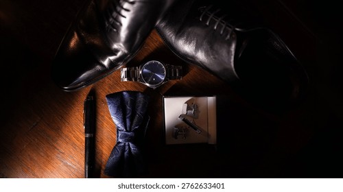 Flat lay of elegant men’s accessories including polished black leather dress shoes, a wristwatch, cufflinks, a bow tie, and a pen arranged on a wooden surface. Dramatic lighting creates a sophisticated and luxurious atmosphere, ideal for concepts related to fashion, business style, formal events, and men’s grooming.     
