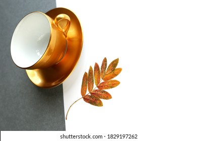 Flat lay with empty coffee cup and autumn yellow leaves with copy space at right. Large golden cup in antigravity position on the geometric grey and white background. Minimalism concept