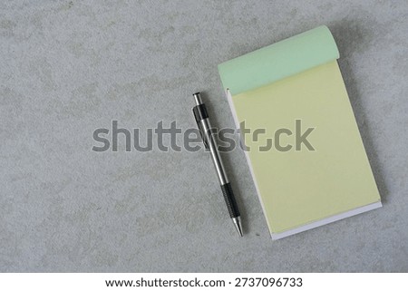Flat lay of Empty light yellow note book and silver pen on grey surface