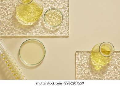 Flat lay of erlenmeyer flasks, petri dish and a test tube with spiral pipe inside containing yellow liquid. Cosmetic laboratory research and development content