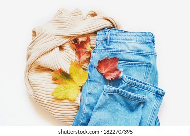 Flat Lay Fall And Winter Season Fashion Photography. Beige Sweater, Blue Jeans And Yellow, Red Leaves. Fashionable Autumn Outfit