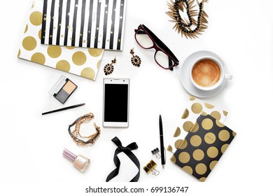 Flat Lay Fashion Feminine Home Office Workspace With Phone, Cup Of Coffee, Stylish Black Gold Notebooks, Cosmetics And Jewelry On White Background. Women's Business Desk Form Above With Space For Text