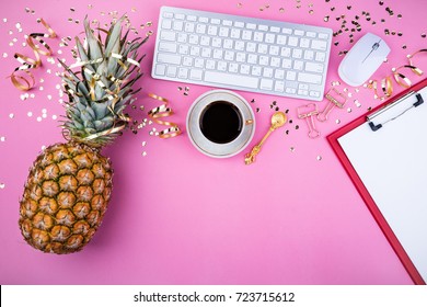 Flat lay fashion feminine home office workspace. Festive female background. Pineapple, coffee cup, golden confetti and clips on pink table. Top view