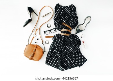 flat lay feminine clothes and accessories collage with black dress, glasses, high heel shoes, purse, watch, mascara, lipstick, earrings on white background.