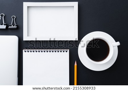 flat lay of fold back clips near notebook, frame and cup of coffee on black