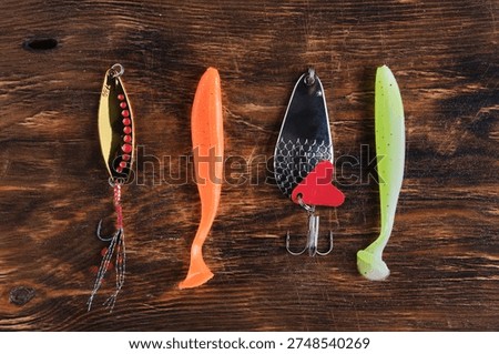 Flat lay four different types fishing lures two metal spoons and two soft plastic baits arranged on textured wooden background