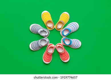 Flat Lay With Four Pairs Of Multicolored Children's Shoes Isolated On A Green Colored Background. Colorful Shoes Arranged In A Circle.