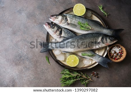 Flat lay fresh raw fish seabass in a plate with ice cubes, rosemary and lime on a dark rustic background. Top view, copy space
