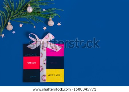 Flat lay gift box shape with a bow of satin ribbon made of shop gift cards, decorated with golden balls christmas tree branch on trending new color Classic blue background. Creative ideas for presents