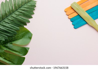 Flat Lay Green Tropical Leaves Palm And Blue And Orange Popsicle Stick On A White Background With Center Copy Space. Minimal Summer Background Concept. Close-up Photo.