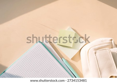 Flat lay of grid notebook with sticky notes, pen and pencil case on beige desk