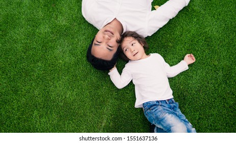 Flat lay of Happy Asian father smiling up to the camera and curious toddler boy looks at his dad on the grass field with copy space on the left, the concept of happy family or father-son relationship. - Powered by Shutterstock