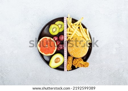 Flat lay of Healthy and unhealthy food from fruits and vegetables vs fast food, sweets and pastry in black plate on gray concrete background. Diet and detox against calorie and overweight lifestyle