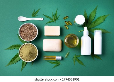 Flat lay with hemp extract products - cosmetics, lotion, face cream, body butter, soap bars, cannabis leaves, seeds, hemp oi, capsules, protein powder, flour on green background. Top view. Copy space.