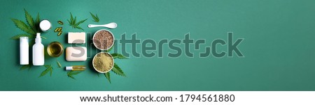 Flat lay with hemp extract products - cosmetics, lotion, face cream, body butter, soap bars, cannabis leaves, seeds, hemp oi, capsules, protein powder, flour on green background. Top view. Banner.