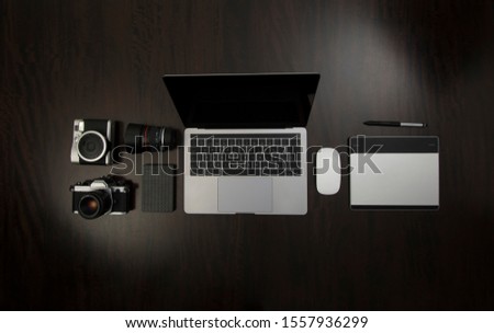 Flat Lay of Hipster freelance designer and analog photographic equipment on a wooden dark desktop with laptop, hard drive, tablet for graphic design and mouse.