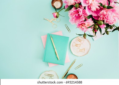 Flat lay home office desk. Female workspace with pink peony flowers bouquet, golden accessories, pink and mint diary on mint background. Top view feminine background.