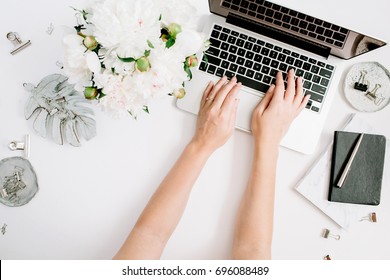 Flat lay home office desk. Women workspace with female hands, laptop, white peony flowers bouquet, accessories, marble diary. Top view feminine background. Girl working on laptop.