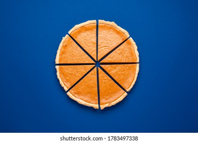 Flat lay with a home-baked pumpkin pie on a dark blue colored background. Pumpkin pie sliced in eight pieces. Homemade thanksgiving dessert.