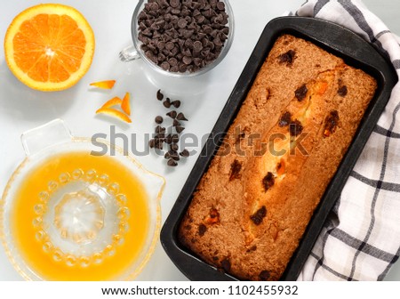 flat lay image of chocolate and orange cake in a baking tin with choc chips by the side  light background 