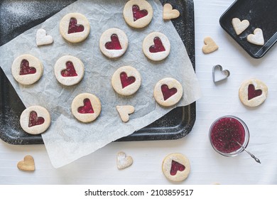 Flat Lay Image Of Heart Shaped Linzer Jam And Jelly Filled Cookies. Baking Treats Concept Including Jam, Cookie Cutters, Icing Sugar And Baking Sheets In Top Down View. Romance And Love Food Concept.