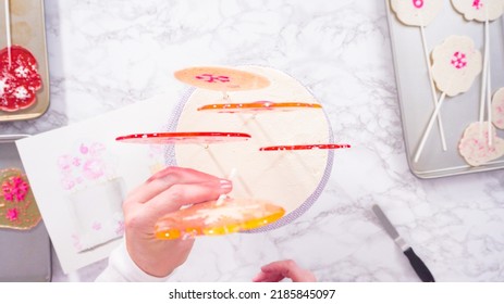 Flat Lay. Inserting Large Lollipops With Snowflakes Into The Tall White Round Cake As A Final Decoration.