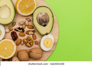 Flat lay ketogenic diet. Аvocado,eggs,lemon,nuts on the wooden cutting board on the green background. Concept of healthy food,top view.Copy space for mock up