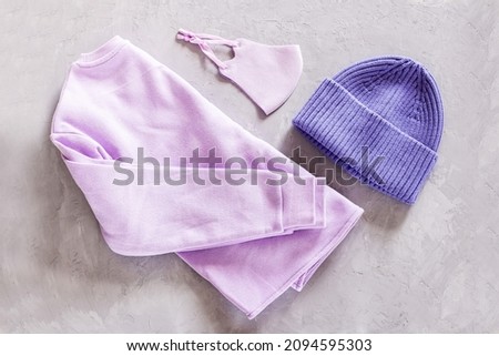 Flat lay of knitted hat and Protective face mask on gray concrete nackground. Color of the year 2022 very peri. Trendy colors concept, mockup with copy space
