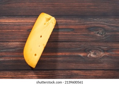 Flat Lay. Large Wedge Of Smoked Gouda Cheese On A Dark Wooden Background.