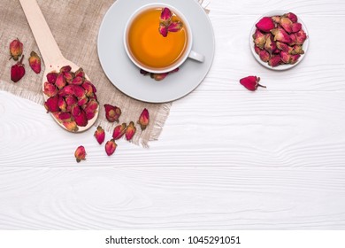 Flat lay layout with herbal tea with rosebuds. White cup with hot tea. A wooden spoon with dried flower buds on a linen napkin. View from above