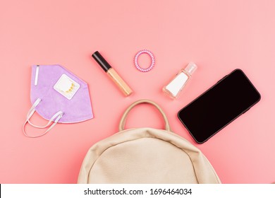 Flat Lay Of Leather Woman Bag Open Out With Face Mask, Sanitizer Hand Gel To Protect From Coronavirus Or COVID-19, Lipstick, Accessories And Smartphone On Pink Background With Copy Space