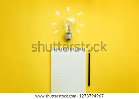 Flat lay of light bulb and empty memo pad and pencil on yellow background with texts. Conceptual brain storming still life.