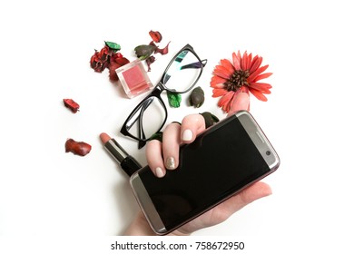 Flat Lay Of  Lipstick, Lip Gloss, Glasses And Mobile Phone In Female Hand Over A White Background