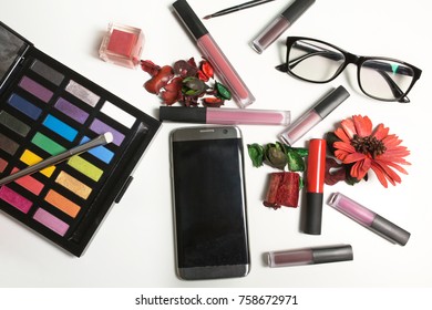 Flat Lay Of  Lipstick, Lip Gloss, Glasses And Mobile Phone On A White Background