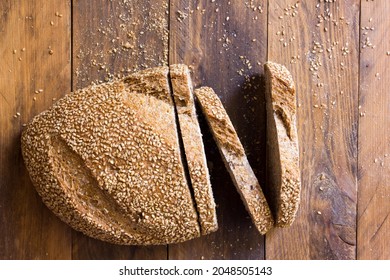 Flat lay of a loaf of wholemeal sourdough bread with cereals, sesame and nuts on a rustic wooden table. Copy space. Wholemeal food concept