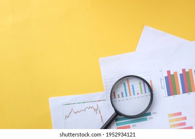 Flat Lay Magnifying Glass And Graph Charts  Document On Yellow Background