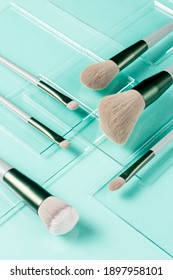 Flat lay of makeup brushes on pieces of glass on the turquoise background. Cosmetic products, side view