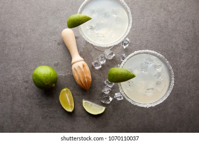 Flat Lay With Margarita Cocktails With Pieces Of Lime, Ice Cubes And Wooden Squeezer On Grey Tabletop