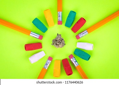 Flat Lay Of A Marijuana Bud In A Circle Of Pencils And Erasers, In Colorful Display Of Drugs And School